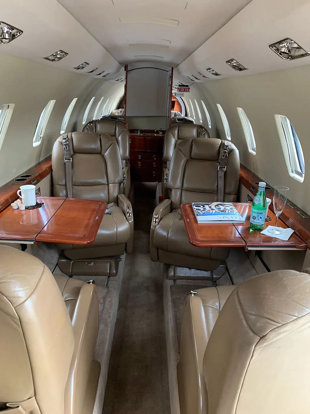 View of the aircraft cabin interior with tan leather seats, fold-out tables, and refreshments.