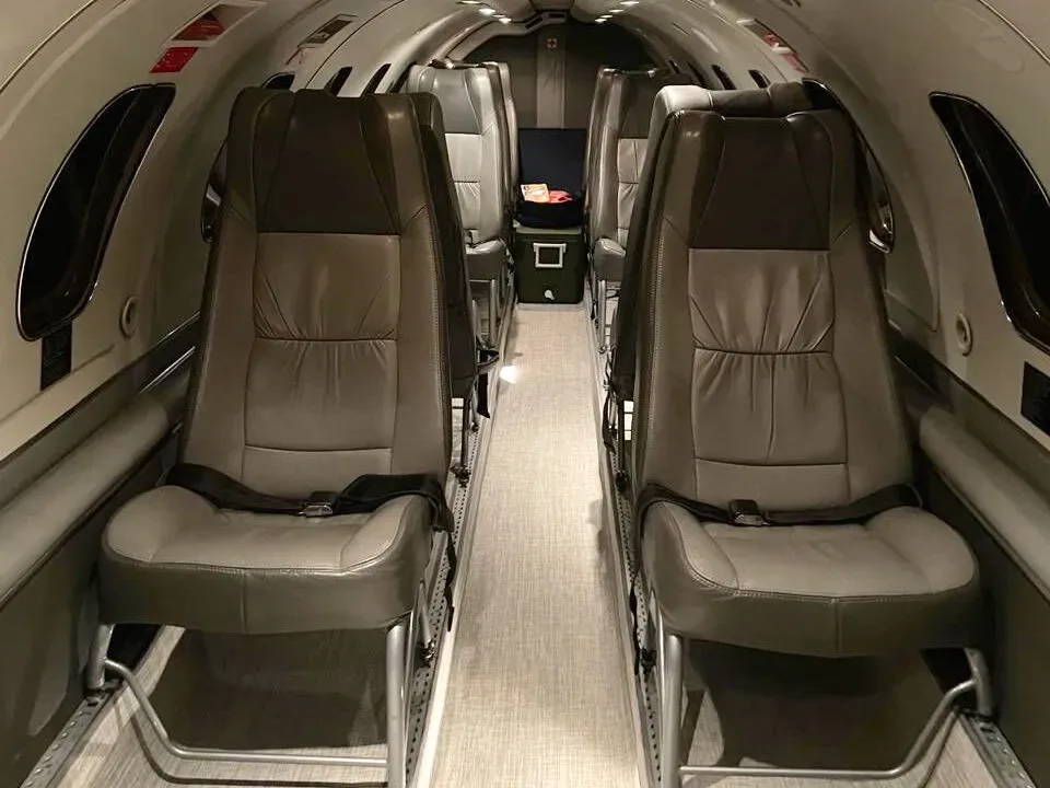 The interior cabin of an aircraft with two rows of grey leather seats facing forward, and a cooler box in the aisle.