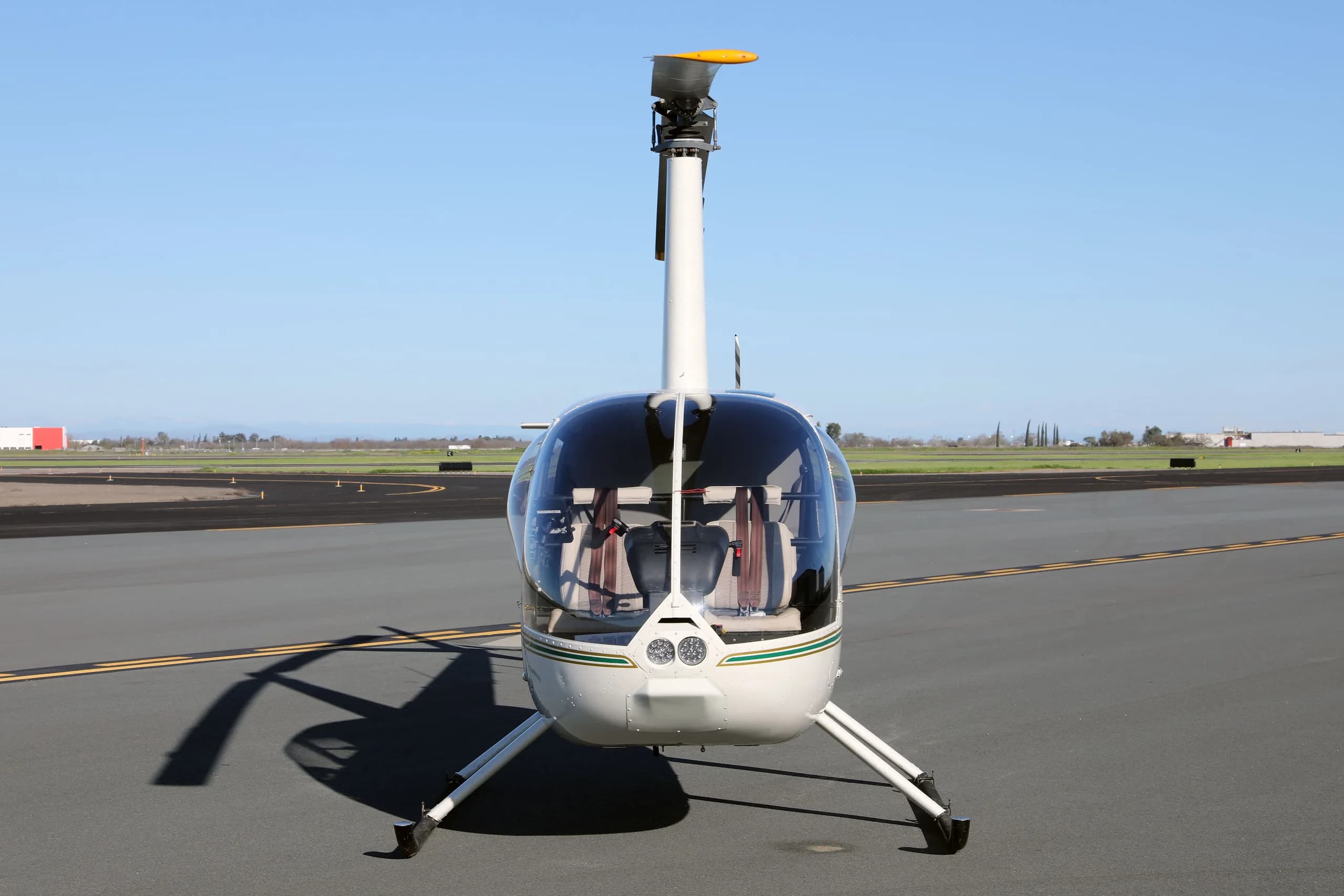 Front view of a white Robinson R44 Raven II helicopter with a green stripe, registration N7527G, parked on an airfield.