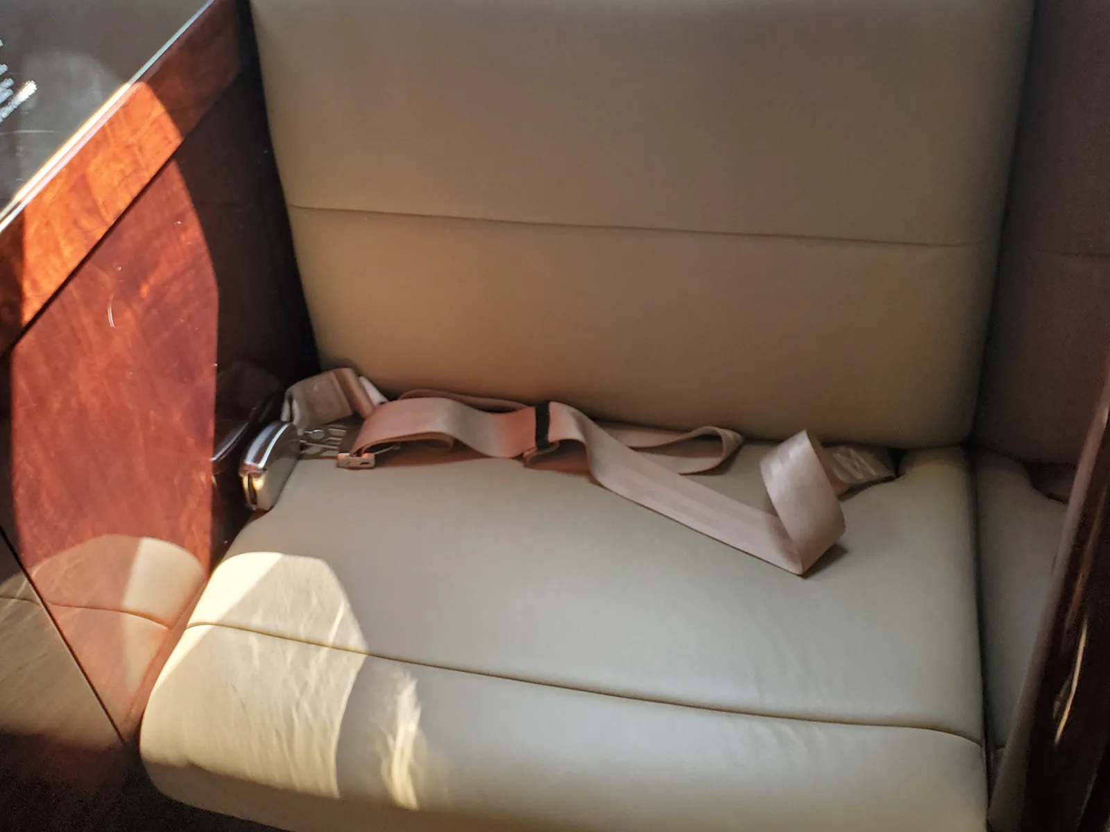 A light beige leather aircraft seat with a seatbelt, next to a polished wood panel.