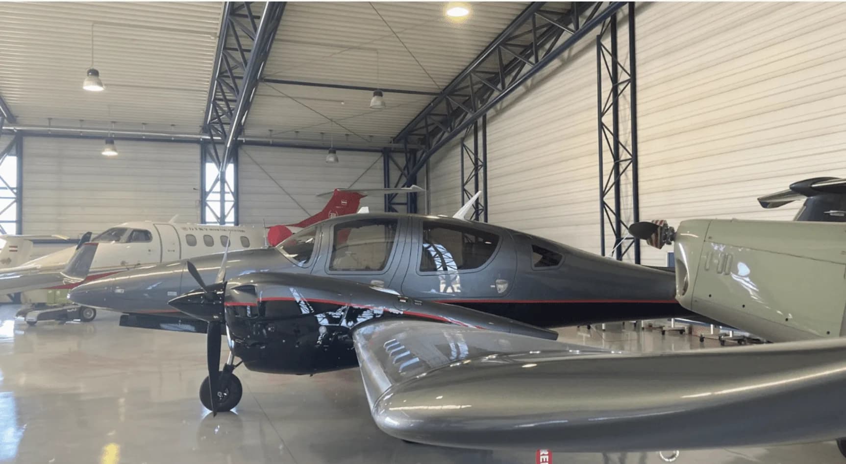 A grey Diamond DA62 twin-engine aircraft with red pinstripes parked inside a hangar.