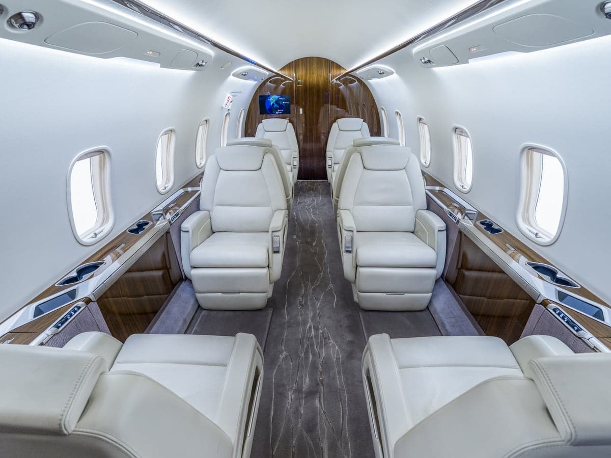 View of the aircraft's interior with white leather seats and wood trim.