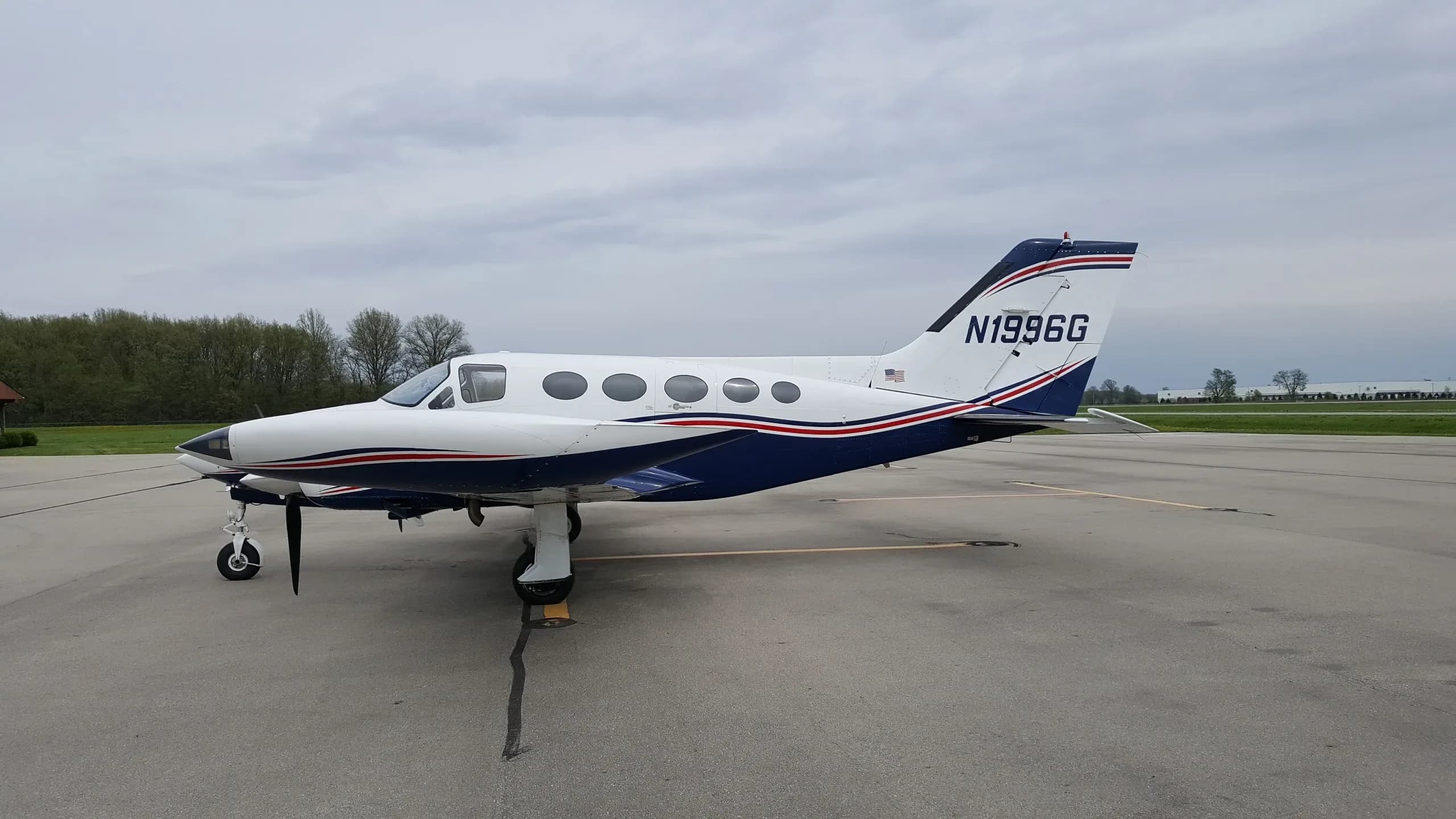 A close-up view of the wing and rear fuselage of a white and blue Cessna 414 Chancellor aircraft (N1996G) with its door open.