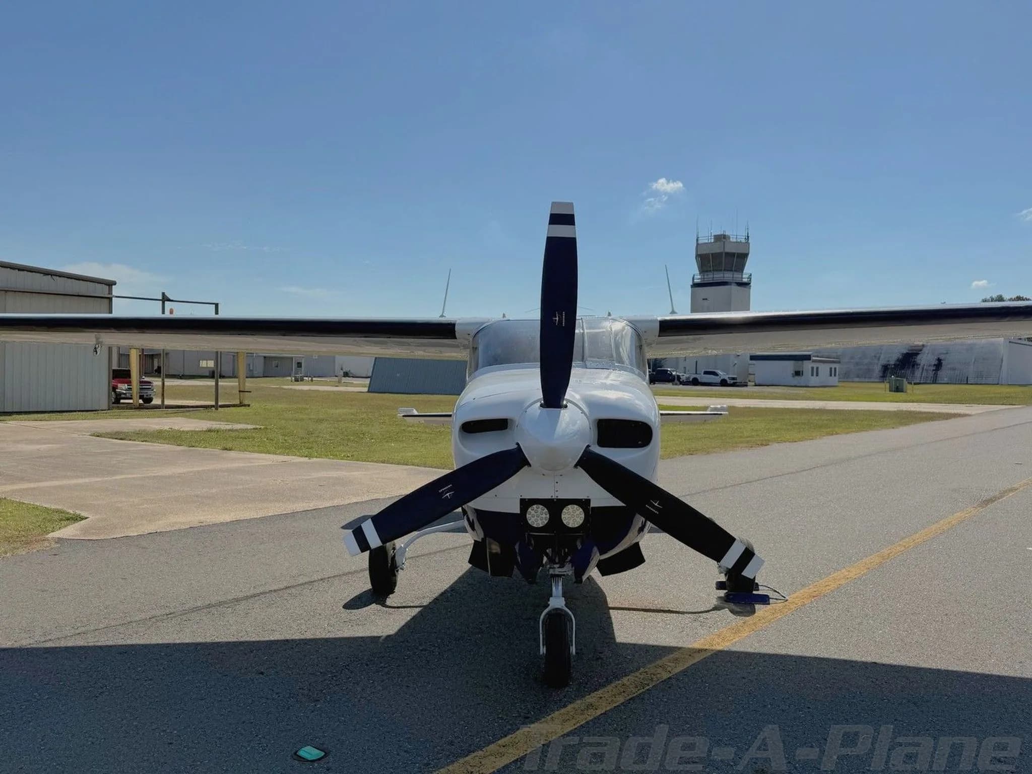 A front view of a white and blue Cessna 210 Centurion aircraft (N403S) on an airfield with a control tower in the distance.