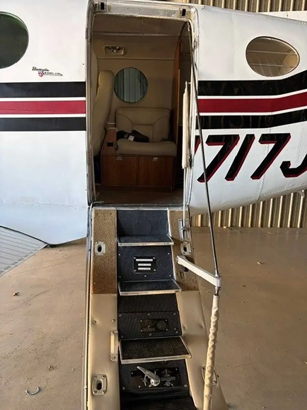 The open airstair door of a white and red Beechcraft King Air C90 aircraft, showing steps leading into the cabin.