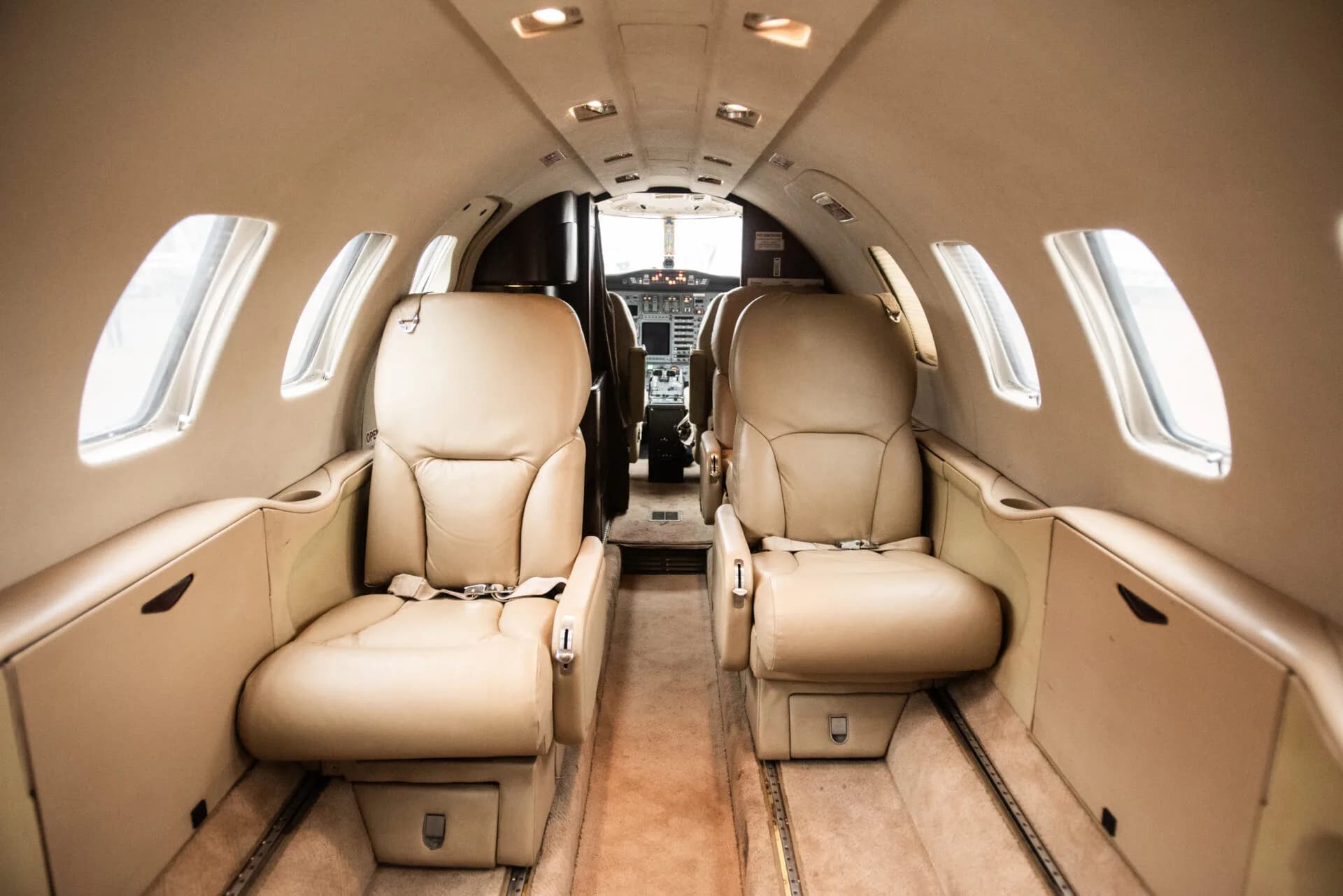 The interior cabin of a business jet with tan leather seats, looking towards the cockpit.