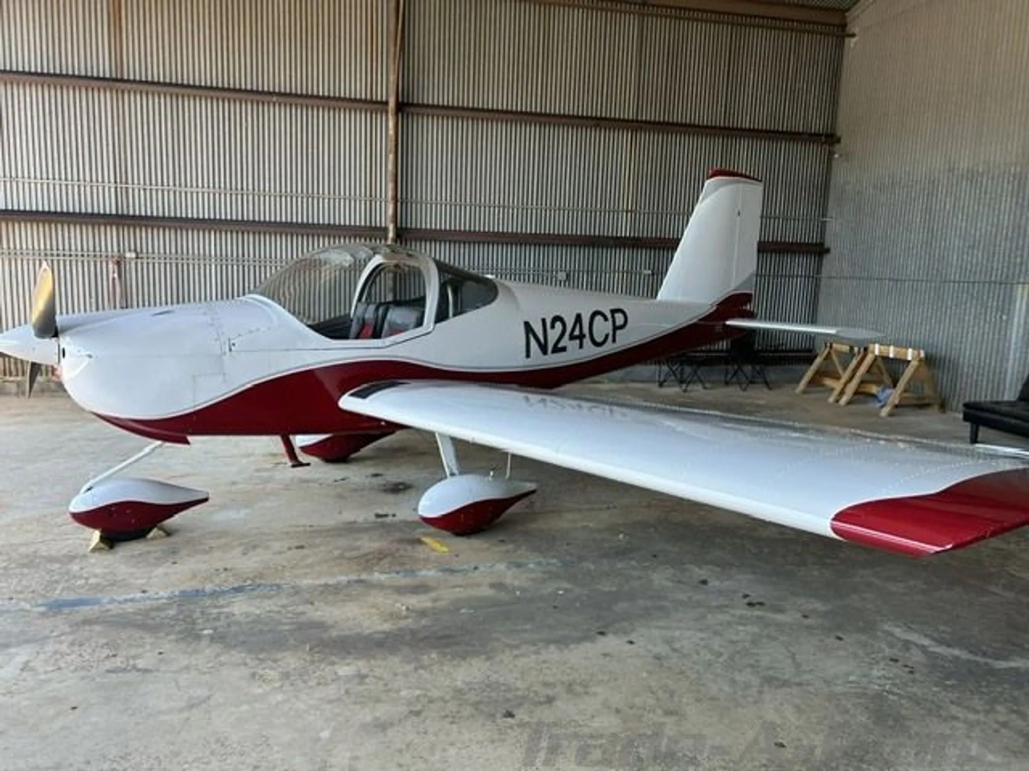 A white and red Van's RV-12 aircraft, N24CP, is parked inside a hangar.