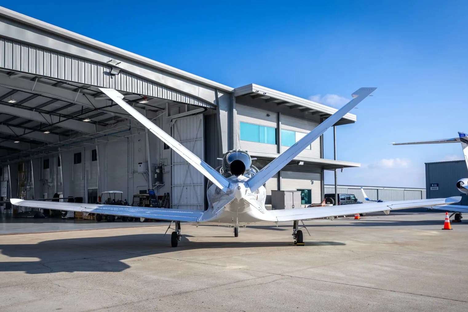 A rear view of a white and dark grey Cirrus Vision Jet (N82WF) parked outside a hangar, showing its single engine.
