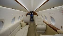 Interior view of the aircraft cabin with white leather seats and tables set with food and drinks.