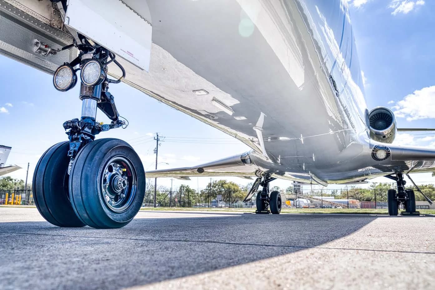 A low-angle view of the main landing gear of a silver business jet on an asphalt surface.