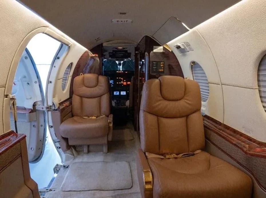 Aircraft interior with two leather seats and an open doorway to the cockpit.