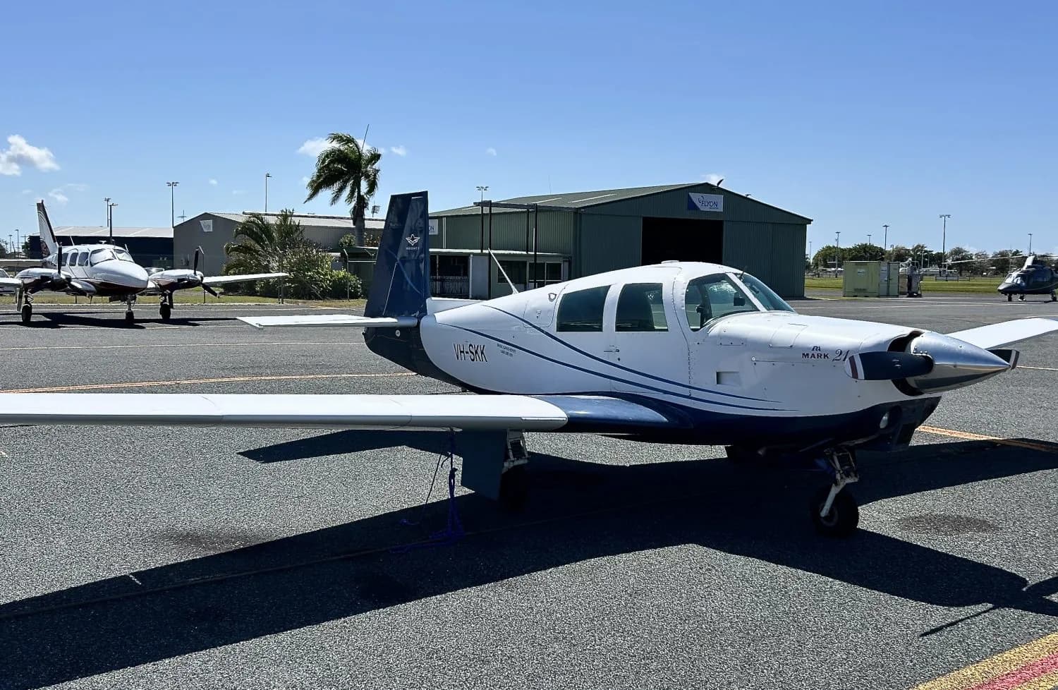 A white and blue Mooney M20J aircraft parked on the tarmac.