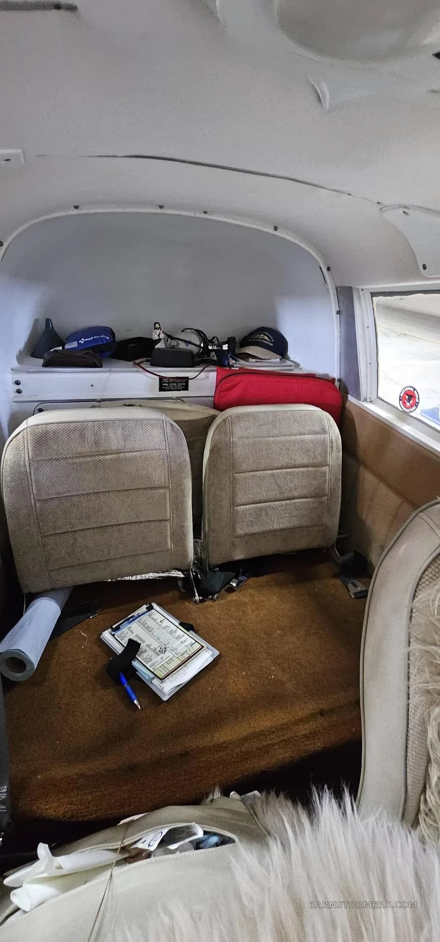 The beige rear cabin seats of a small aircraft, with items stored on the shelf behind them.