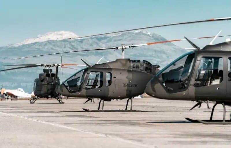 Several helicopters are parked on a tarmac with a mountain in the background.