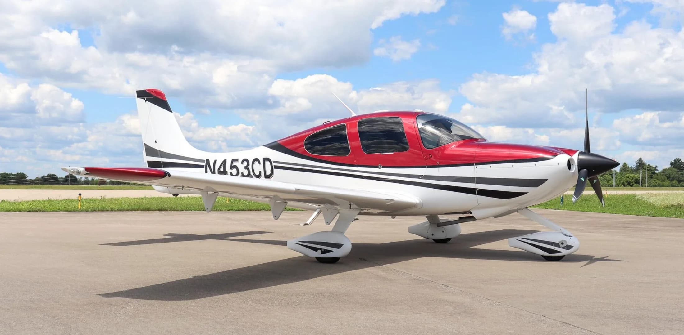 A side view of a white and red single-engine aircraft with tail number N453CD parked on an airfield.