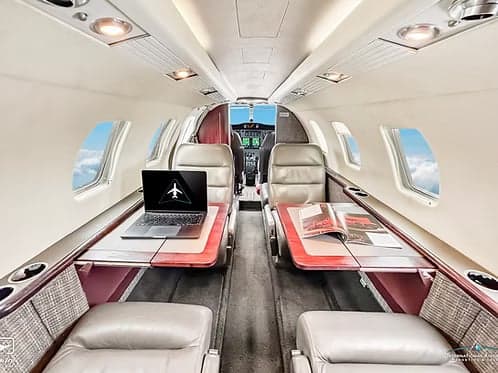 View of the aircraft interior, showing leather seats, tables, and a laptop.