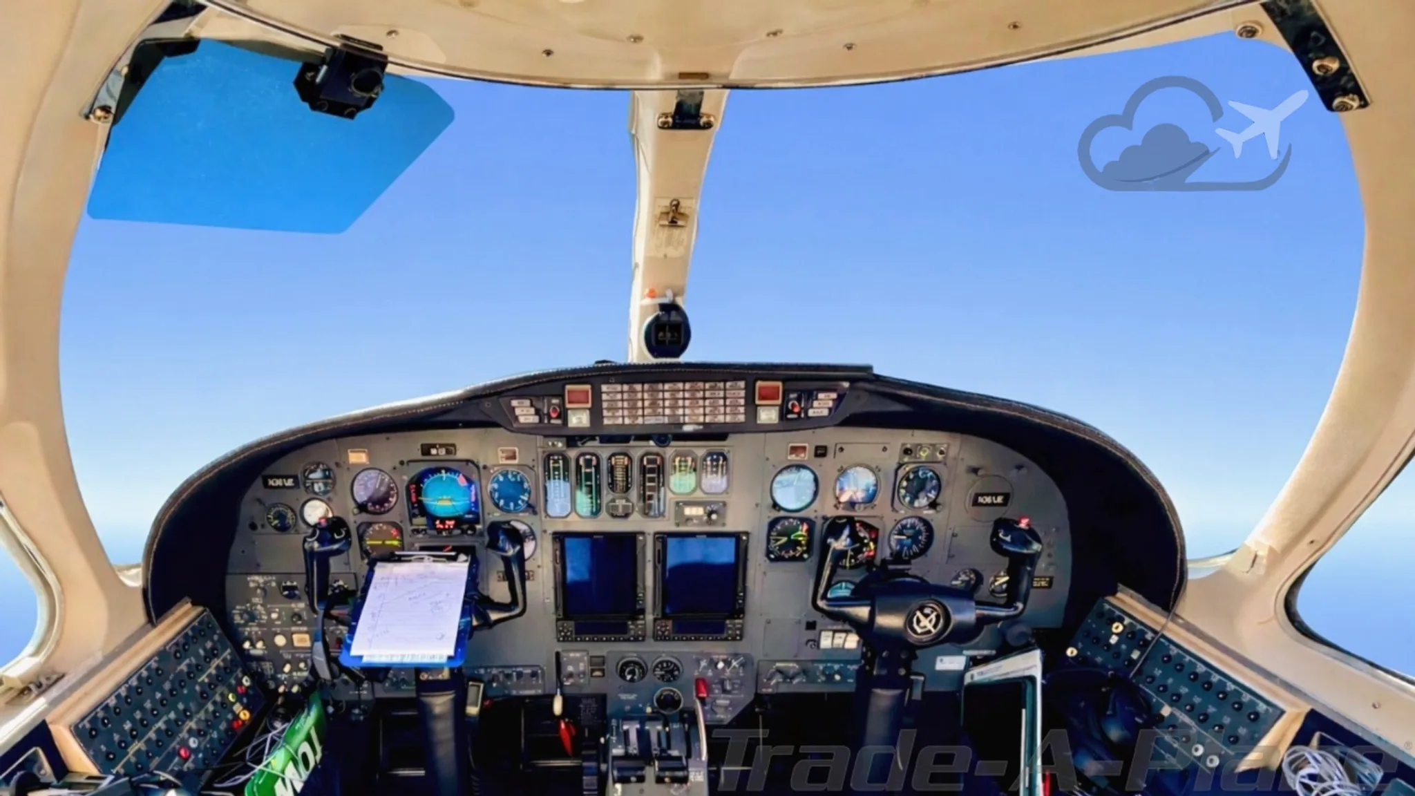 The cockpit of a business jet with a detailed instrument panel and controls, viewed through the windshield.