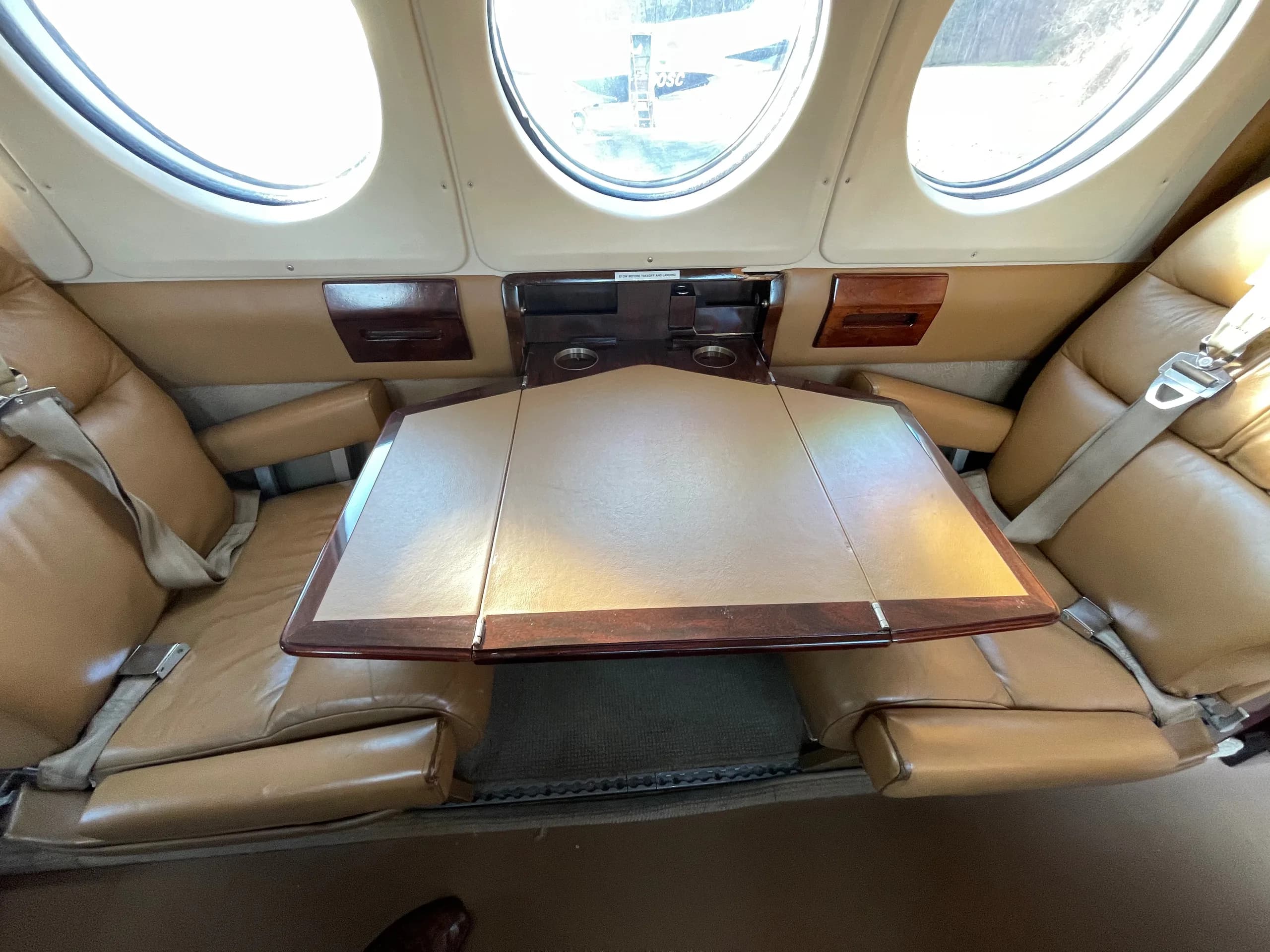A fold-out table between two tan leather seats in the cabin of a private aircraft.
