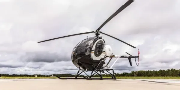 A black and white MD 500 series helicopter, registration N578WT, parked on an airfield under a cloudy sky.