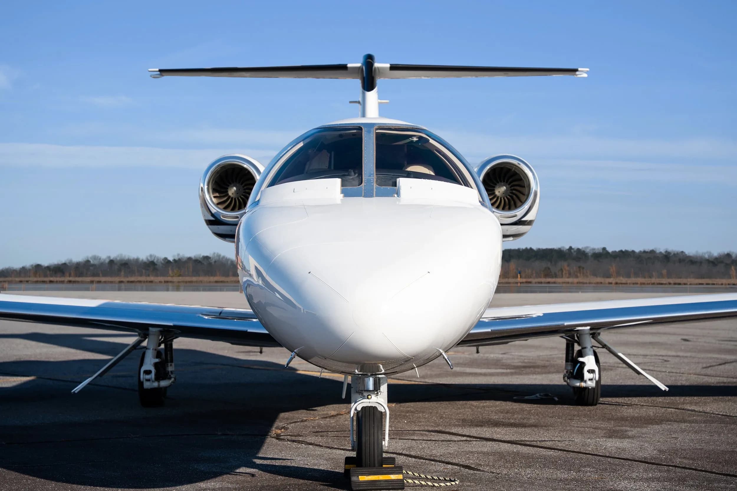 Head-on view of a white business jet with two engines on the tail, parked on an asphalt runway.