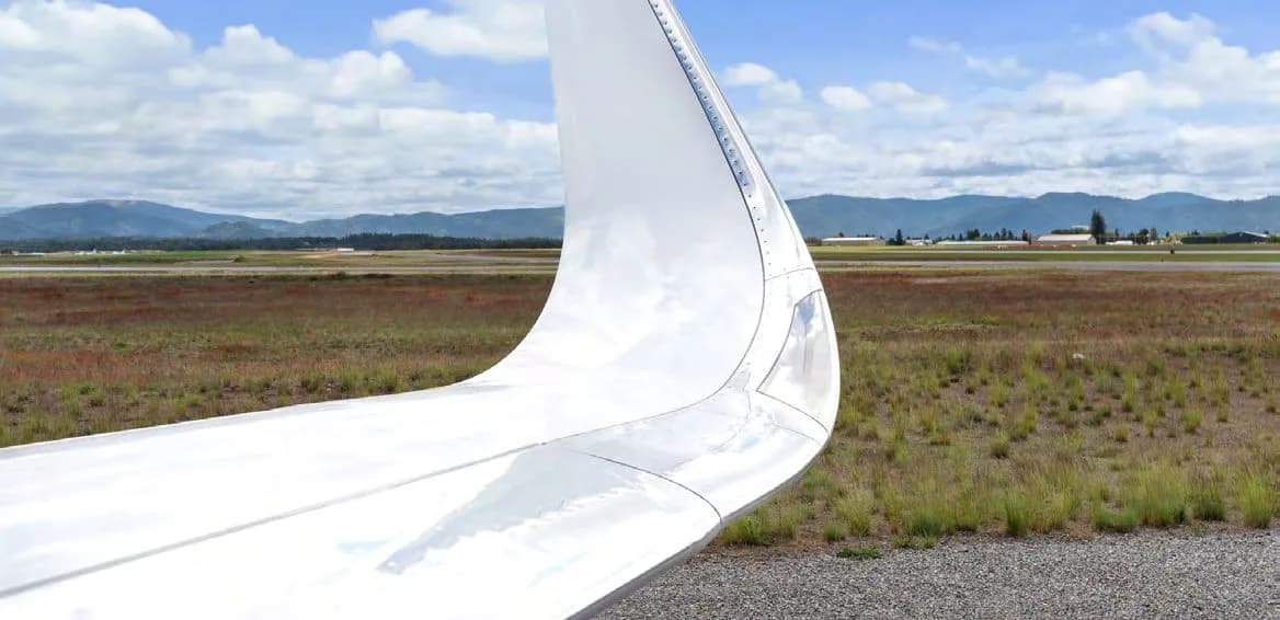 A view over the wingtip of a business jet, showing the airfield and distant mountains.