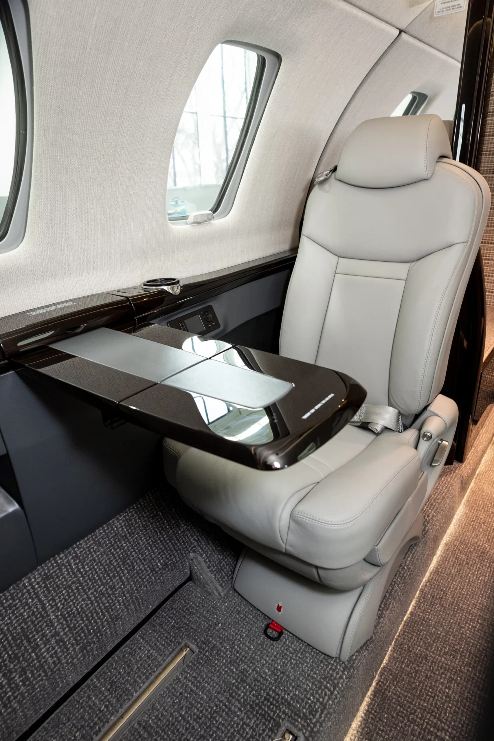 A close-up view of a light gray leather seat and a dark wood fold-out table inside a private jet cabin.