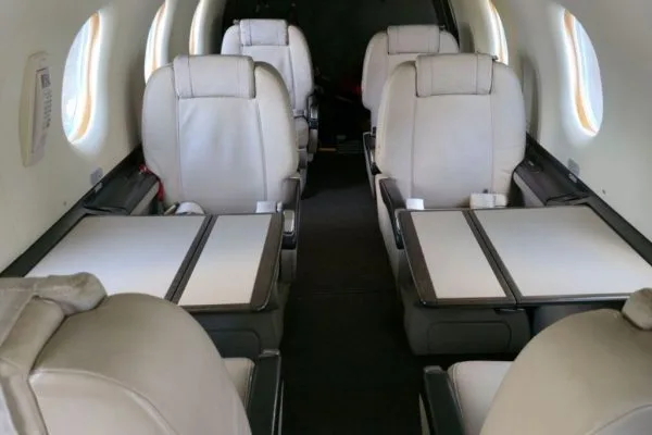 The aircraft's interior cabin with light-colored leather seats and fold-out tables.