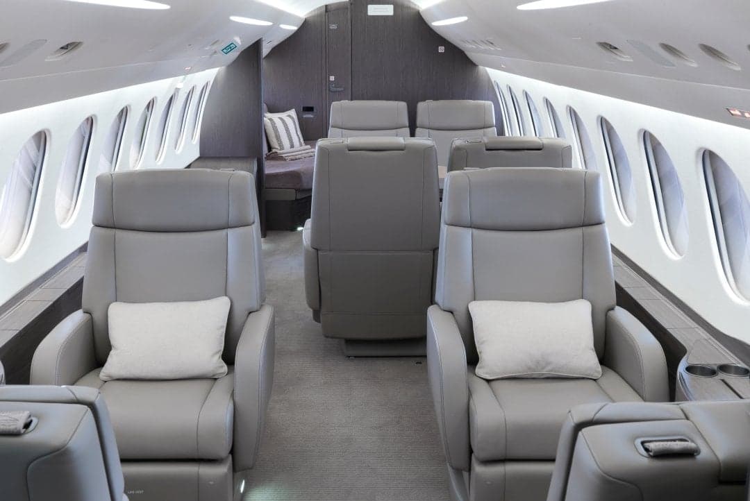 Interior of the aircraft featuring gray leather seats and a bed in the background.