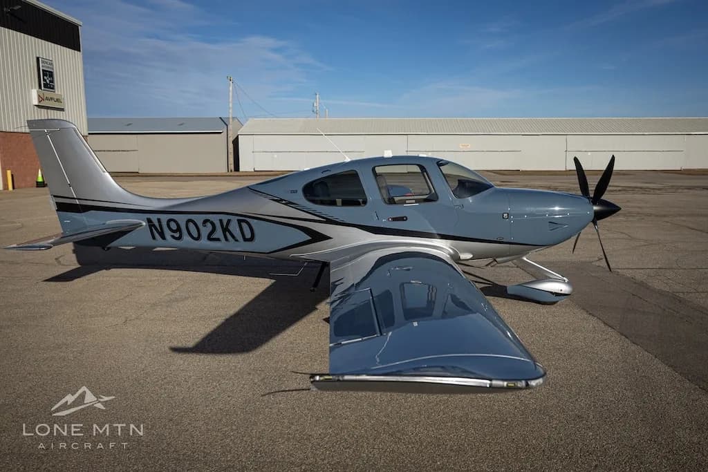 An elevated side view of the Cirrus SR22T aircraft, N902KD, in blue and silver, on an airfield.