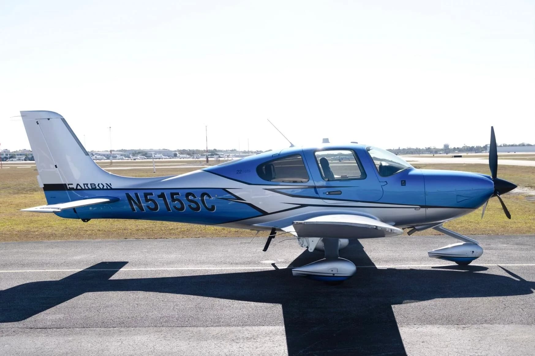 A side view of a blue and silver Cirrus SR22 aircraft (N515SC) parked on an airfield under a clear sky.