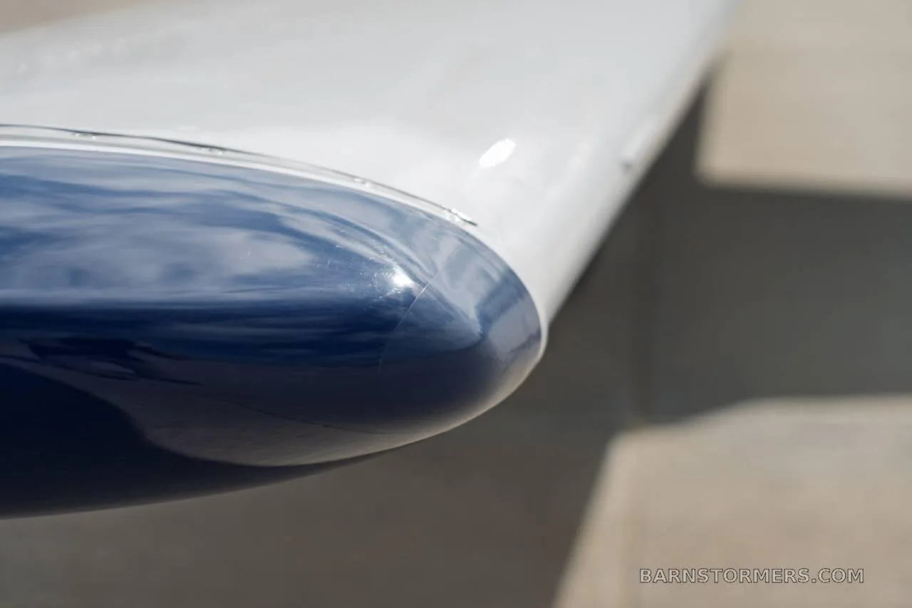 A close-up view of the blue and white wingtip of a small aircraft, showing the smooth surface.
