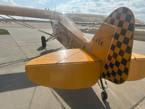 Rear view of a yellow Legend Cub aircraft showing its tail with a black and yellow checkered pattern.