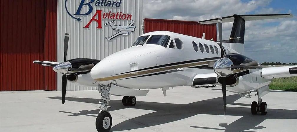 King Air aircraft parked in front of a hangar with the Ballard Aviation logo.
