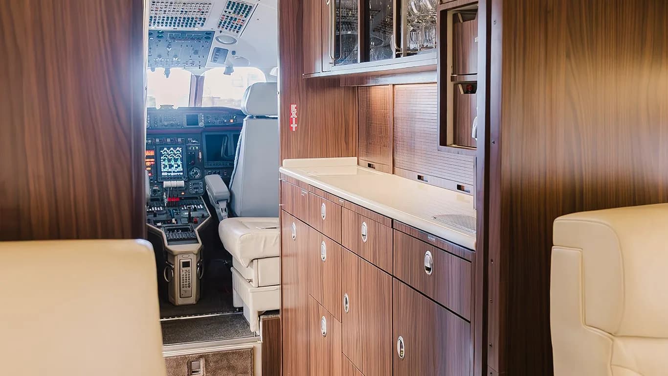A view of the aircraft galley with dark wood cabinetry, looking towards the cockpit.