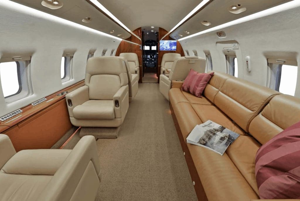 The spacious interior cabin of a business jet, featuring beige leather seats and a long sofa.