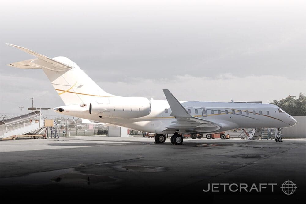 Side view of a white Bombardier Global Express with gold accents parked on the tarmac.
