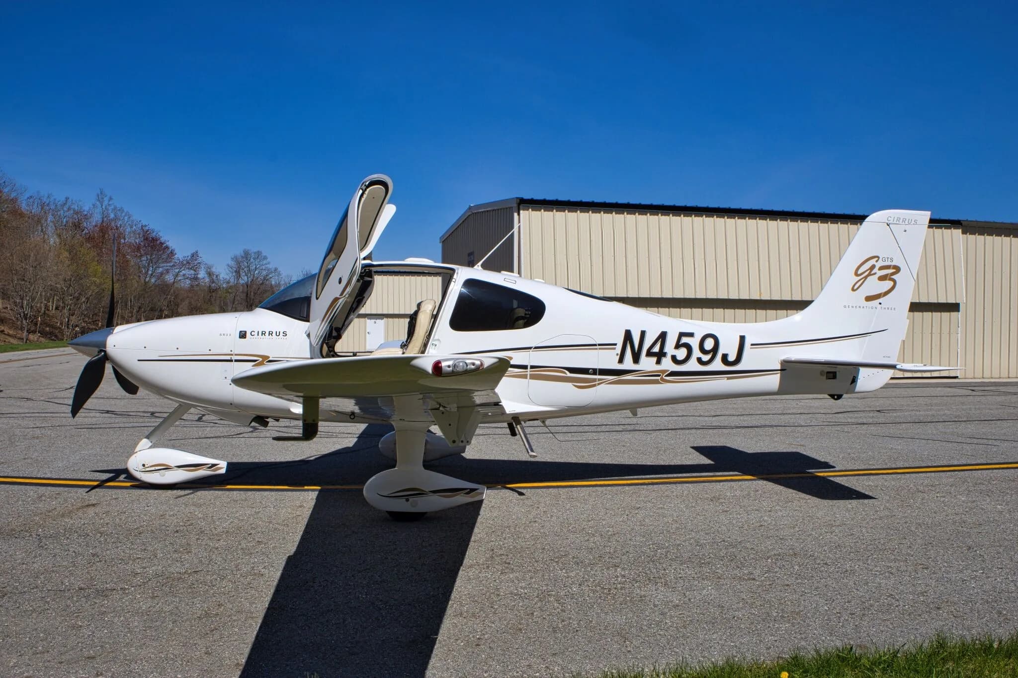 A side view of the white Cirrus SR22 GTS Generation Three aircraft (N459J) with both gull-wing doors open, parked on an airfield.