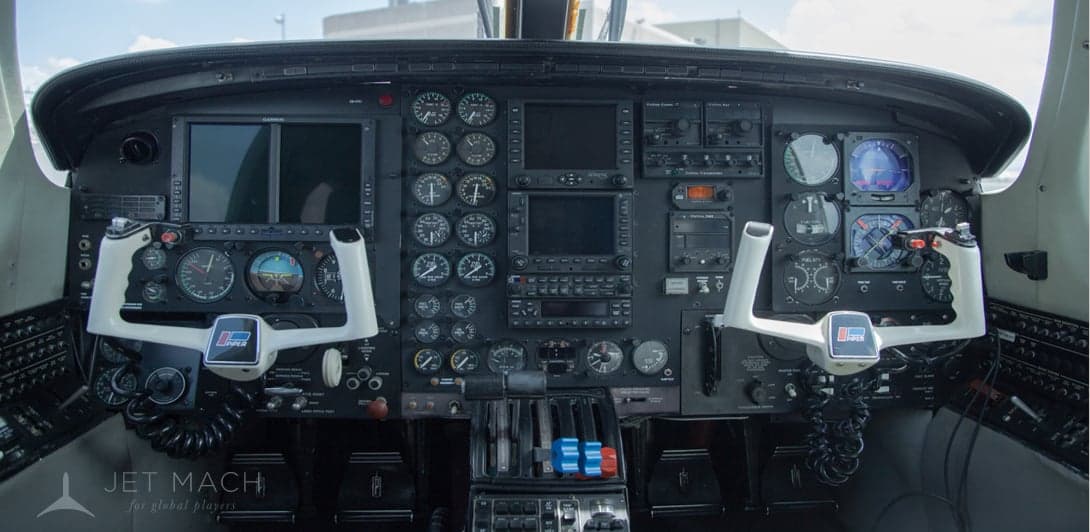 The cockpit of a twin-engine aircraft, showing the instrument panel with two yokes, gauges, and screens.