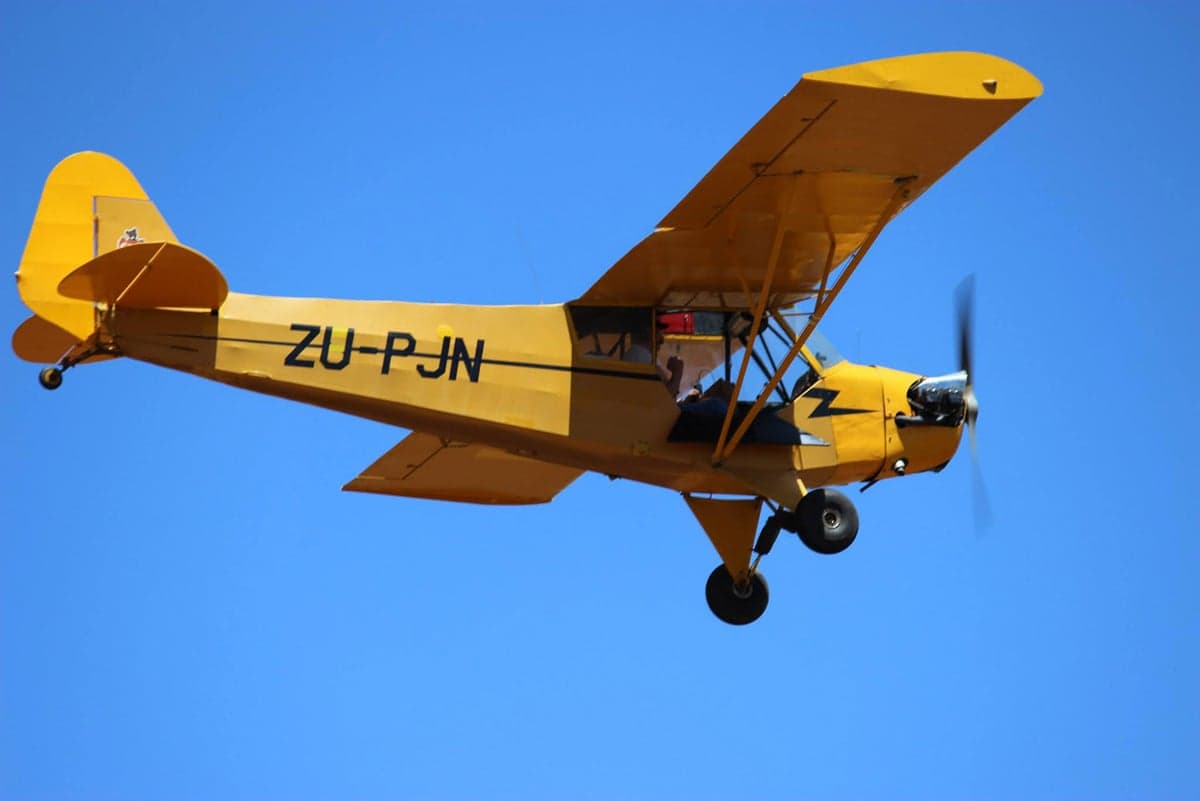 A yellow Piper Cub in flight against a clear blue sky.