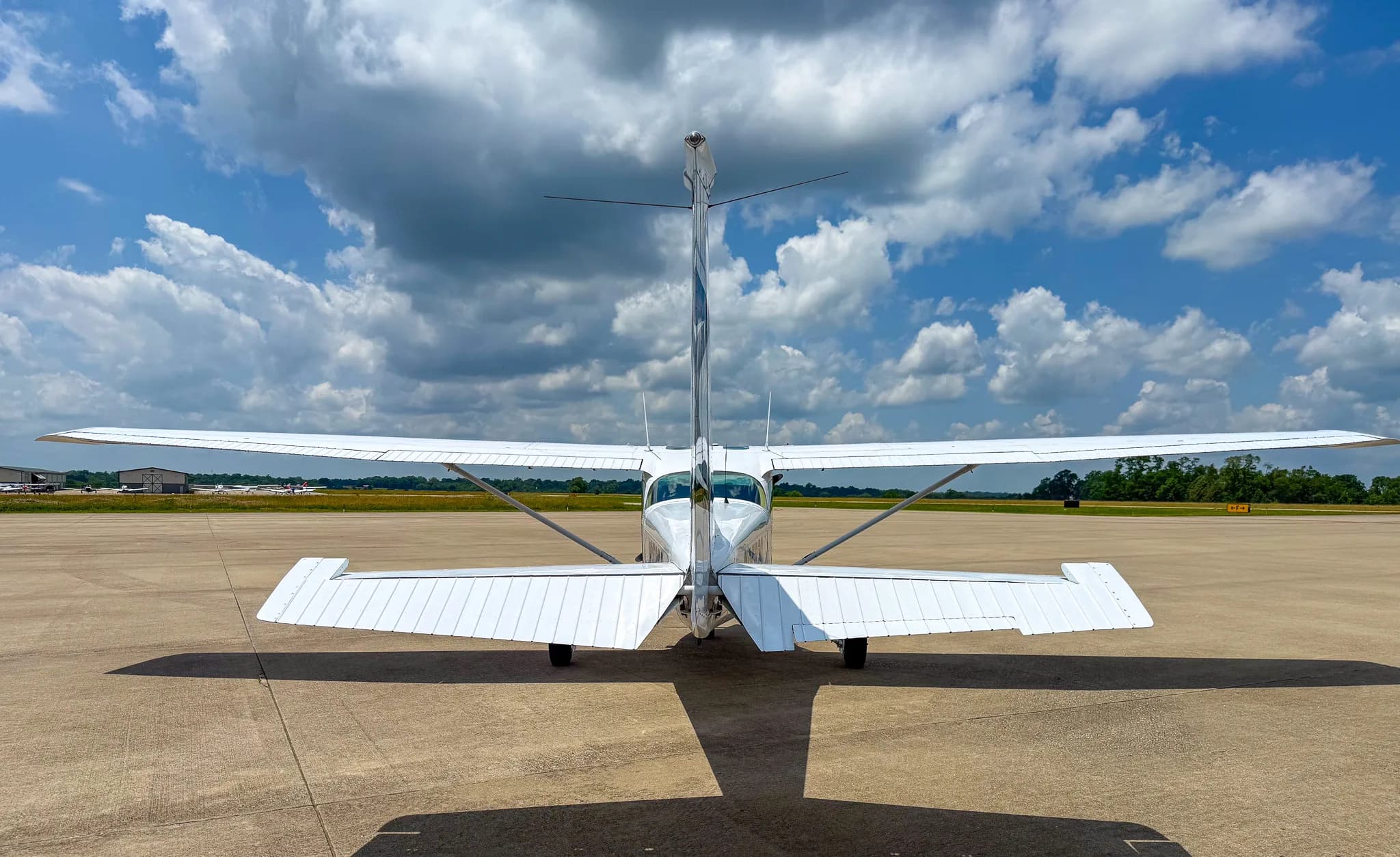 Rear view of a white Cessna 172 parked on an airfield under a cloudy sky.
