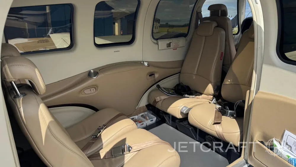 A view of the tan leather passenger seats in the rear cabin of a small aircraft, with windows showing the exterior.
