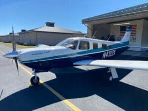 Piper Saratoga II HP aircraft with blue and white paint scheme parked outside a hangar.