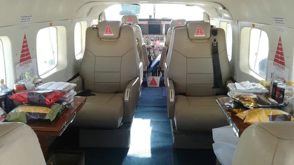 The interior cabin of an aircraft with tan leather seats, small tables laden with snacks, and a view towards the cockpit.
