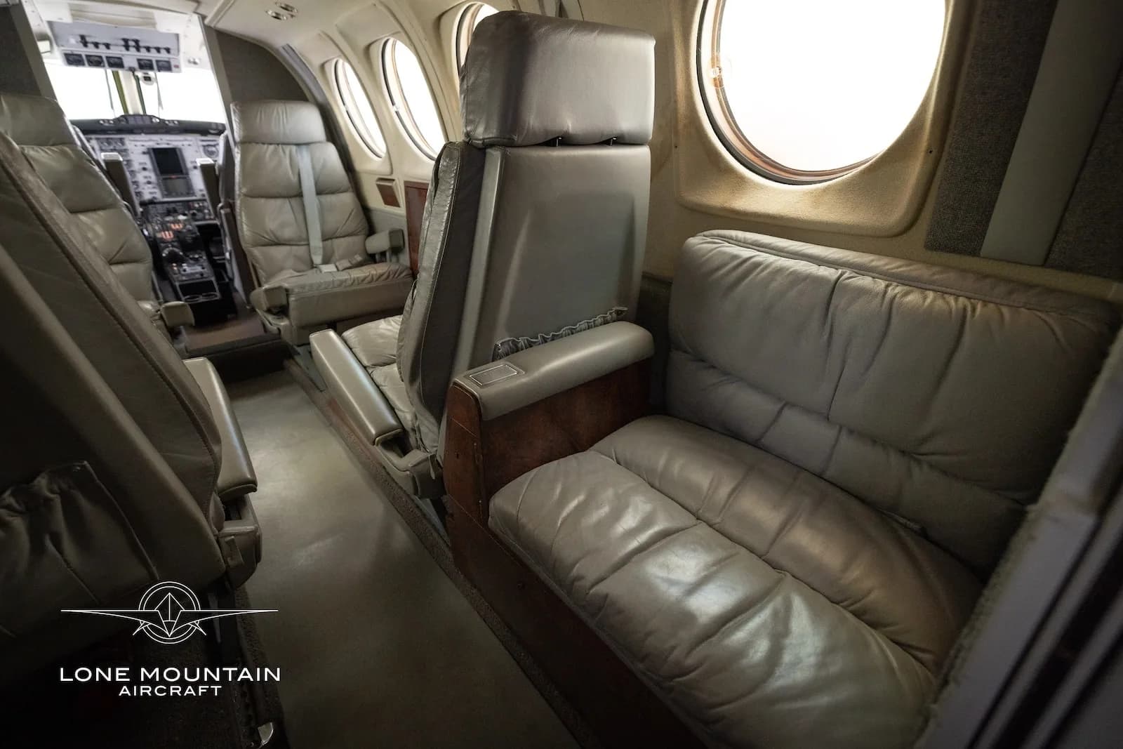 The aircraft's grey leather cabin features a bench seat and individual seats, looking towards the cockpit.