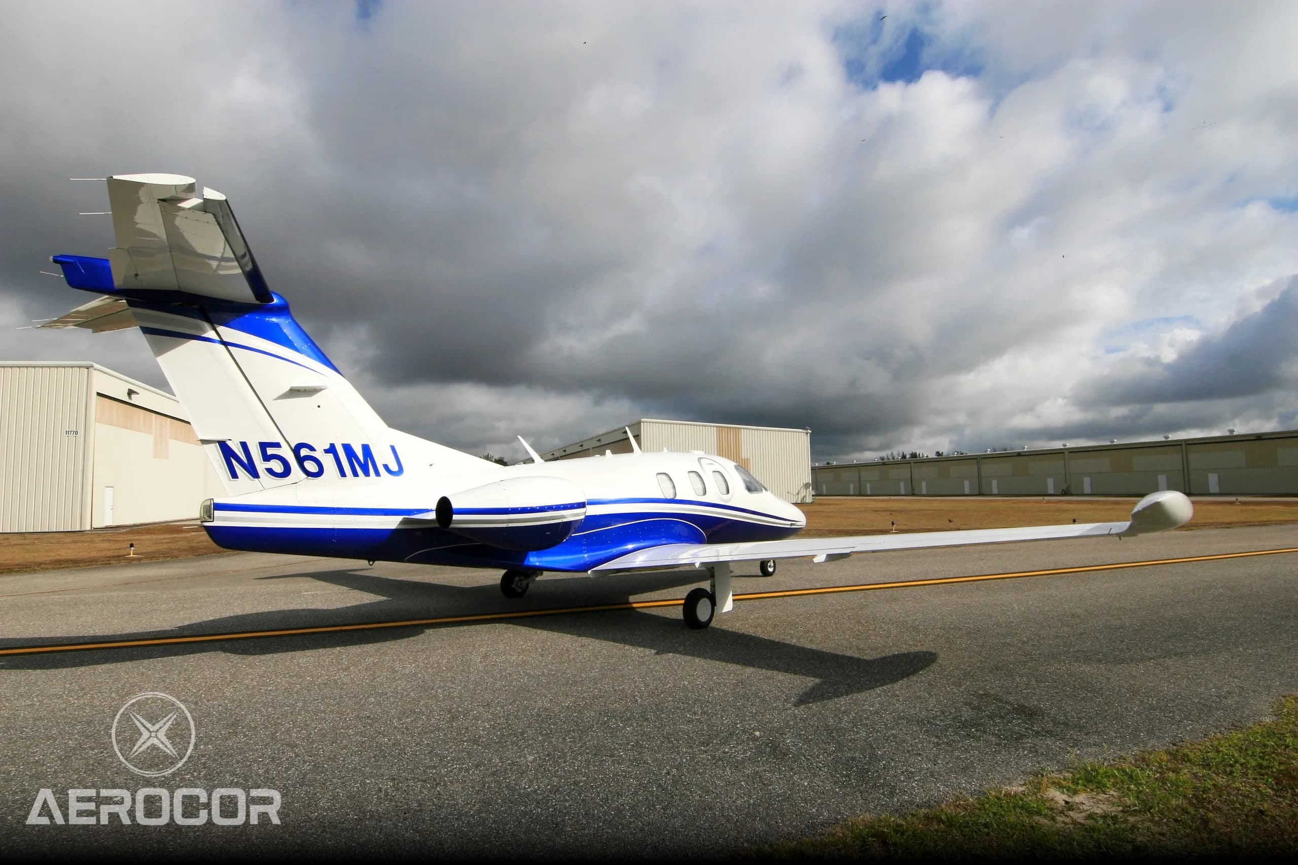 Rear view of a white and blue Eclipse 500 jet, registration N561MJ, parked on an airfield.