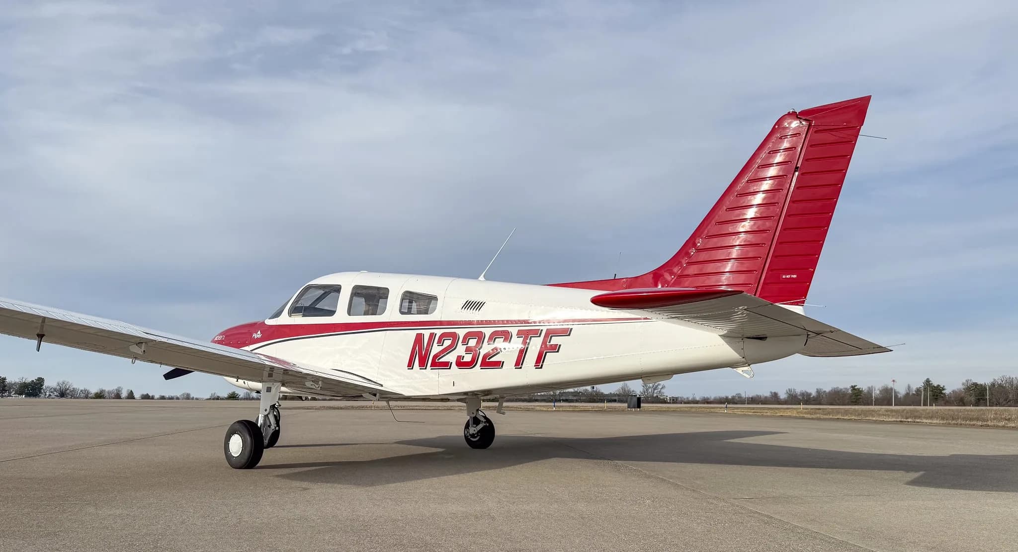 A close-up side view of the rear fuselage and tail of a white and red Piper Archer TX, N232TF, on an airfield.