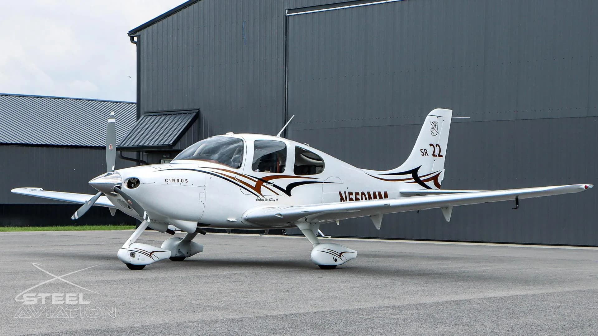 A white Cirrus SR22 aircraft with N559MM registration is parked on the tarmac next to a dark grey hangar.