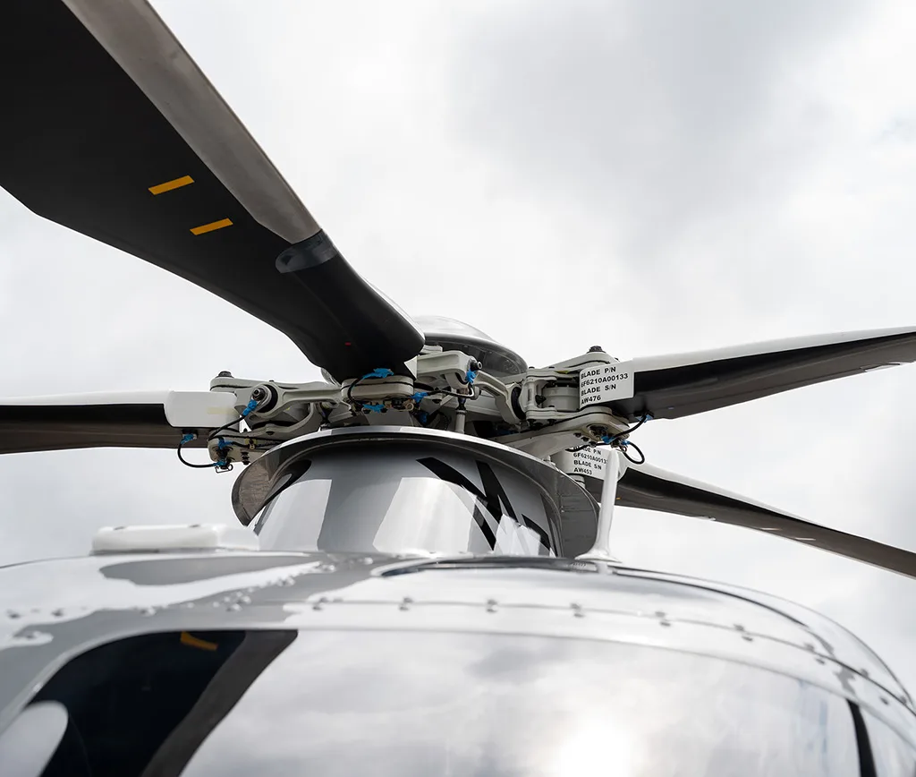 Close-up view of the AgustaWestland AW169 helicopter's main rotor hub and blades against a cloudy sky.