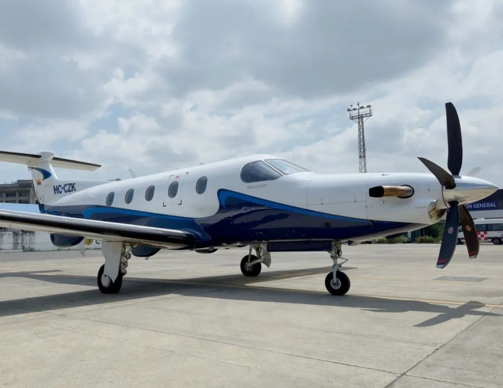 A white and blue Pilatus PC-12 aircraft with registration HC-CZK parked on an airport tarmac under a cloudy sky.