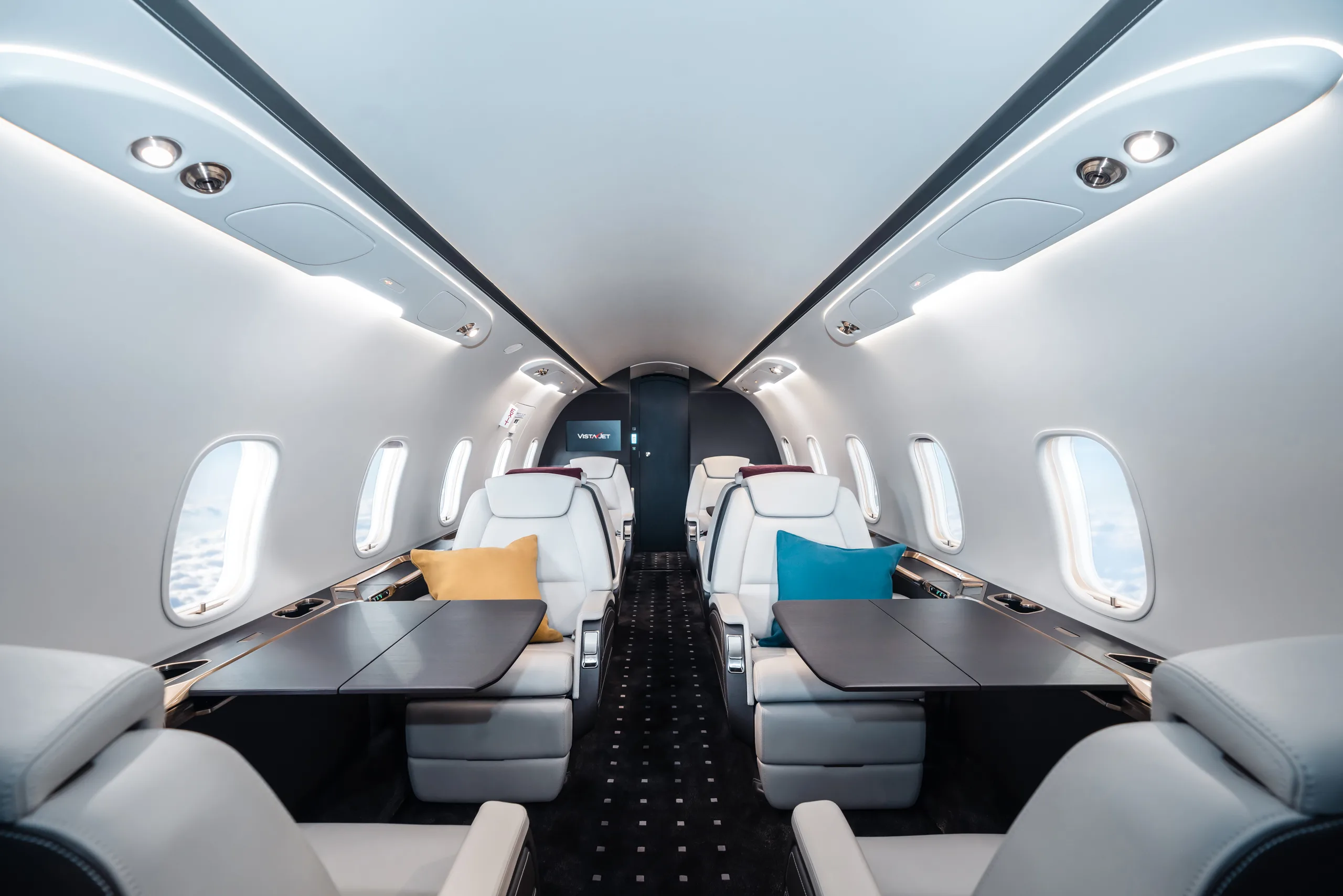 The interior of a jet with white leather seats and tables.